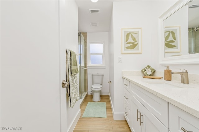 bathroom featuring hardwood / wood-style flooring, a shower with door, vanity, and toilet