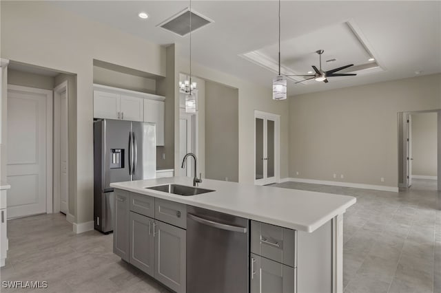 kitchen featuring sink, an island with sink, ceiling fan with notable chandelier, a tray ceiling, and stainless steel appliances