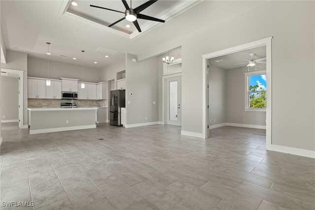 unfurnished living room with ceiling fan with notable chandelier, light tile patterned floors, and a tray ceiling