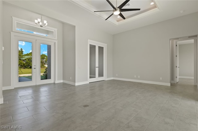 tiled spare room with french doors, ceiling fan with notable chandelier, and a tray ceiling