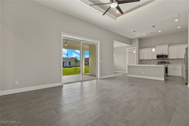 unfurnished living room with ceiling fan, a tray ceiling, and light tile patterned floors