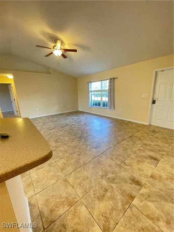 empty room featuring ceiling fan, vaulted ceiling, and light tile patterned floors