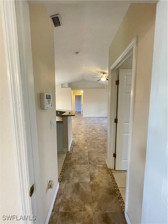 hallway with vaulted ceiling and tile patterned flooring