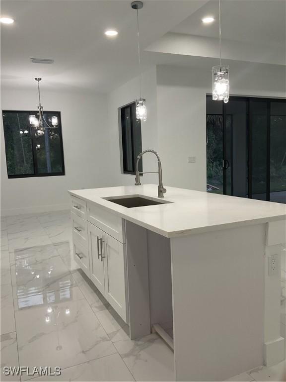 kitchen with white cabinetry, a center island with sink, hanging light fixtures, and sink