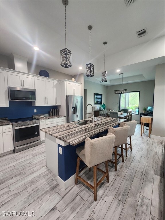 kitchen featuring a center island with sink, light wood-type flooring, appliances with stainless steel finishes, and white cabinets