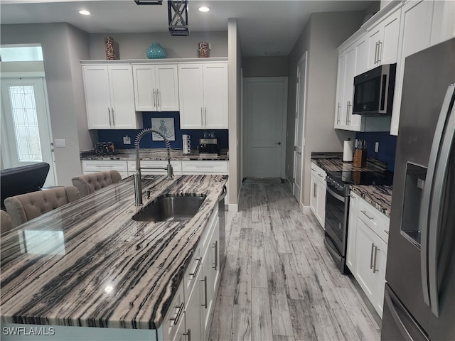 kitchen featuring light wood-type flooring, pendant lighting, white cabinetry, stainless steel appliances, and sink