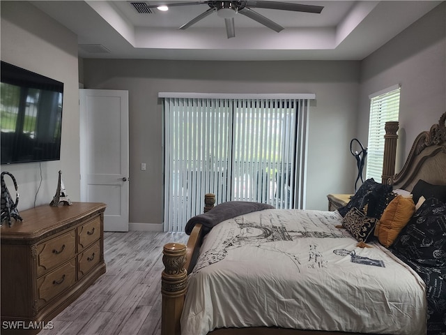 bedroom with light wood-type flooring, ceiling fan, and a raised ceiling