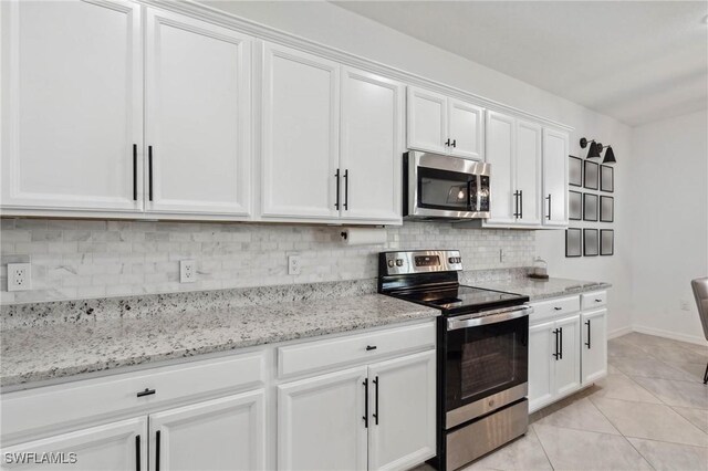 kitchen with appliances with stainless steel finishes, white cabinetry, backsplash, and light tile patterned flooring