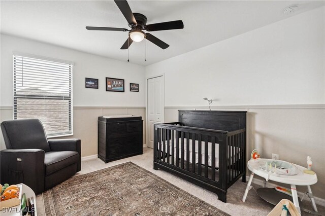 carpeted bedroom featuring ceiling fan and a nursery area