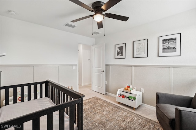 bedroom featuring ceiling fan, a nursery area, and light carpet