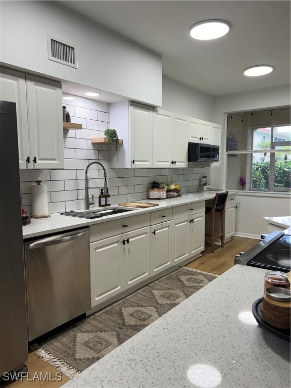 kitchen with backsplash, stainless steel appliances, white cabinetry, sink, and dark hardwood / wood-style floors