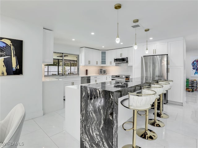 kitchen featuring dark stone counters, decorative light fixtures, a kitchen island, white cabinetry, and stainless steel appliances