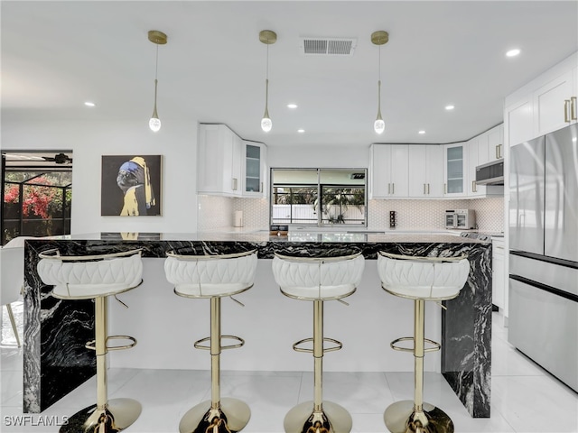 kitchen featuring white cabinetry, ventilation hood, stainless steel fridge, a breakfast bar area, and decorative backsplash