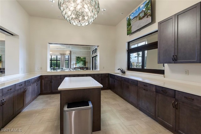 kitchen with a kitchen island, dark brown cabinetry, a chandelier, light countertops, and a sink