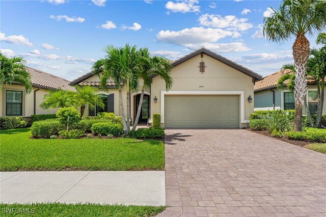 mediterranean / spanish-style house featuring decorative driveway, a tile roof, stucco siding, a front yard, and a garage