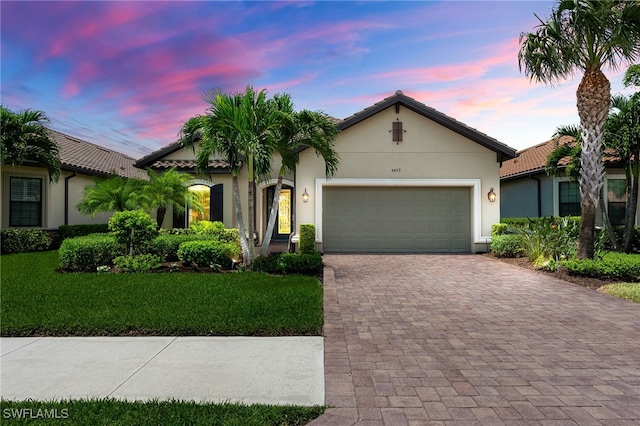 view of front of property with decorative driveway, stucco siding, a lawn, an attached garage, and a tiled roof