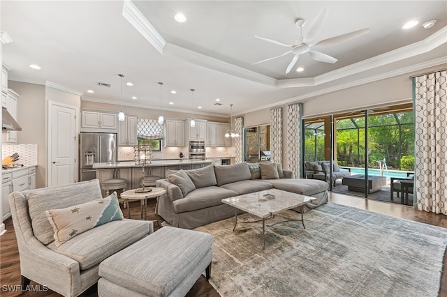 living area with dark wood-style floors, a tray ceiling, visible vents, and crown molding