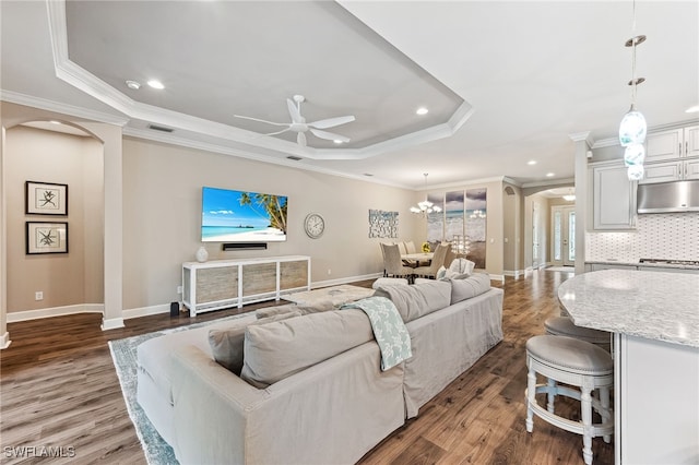 living room with arched walkways, visible vents, ornamental molding, a tray ceiling, and dark wood finished floors