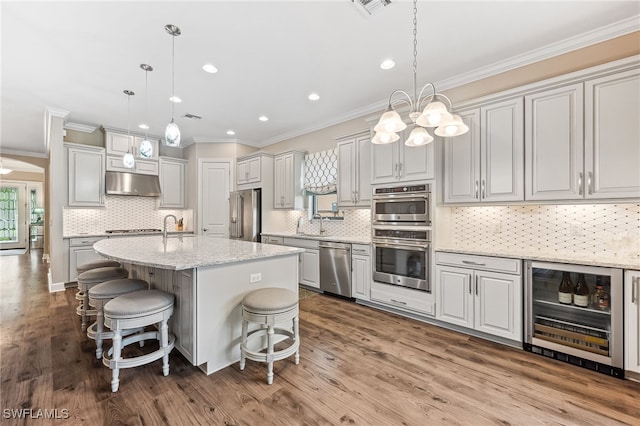 kitchen with under cabinet range hood, beverage cooler, a kitchen island with sink, and pendant lighting