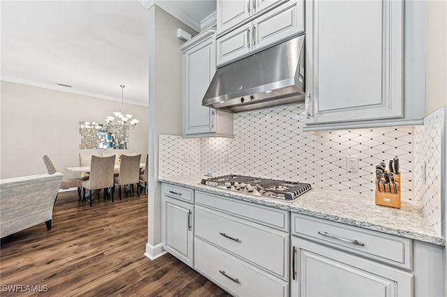 kitchen with dark wood-type flooring, stainless steel gas stovetop, under cabinet range hood, crown molding, and a chandelier