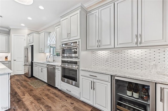 kitchen with beverage cooler, dark wood finished floors, a sink, appliances with stainless steel finishes, and crown molding