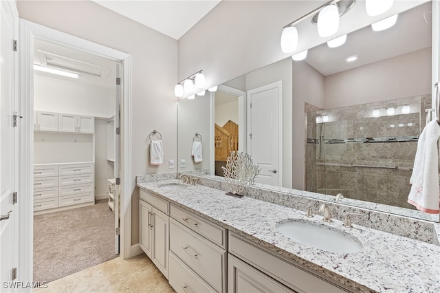 bathroom with a tile shower, double vanity, a walk in closet, and a sink