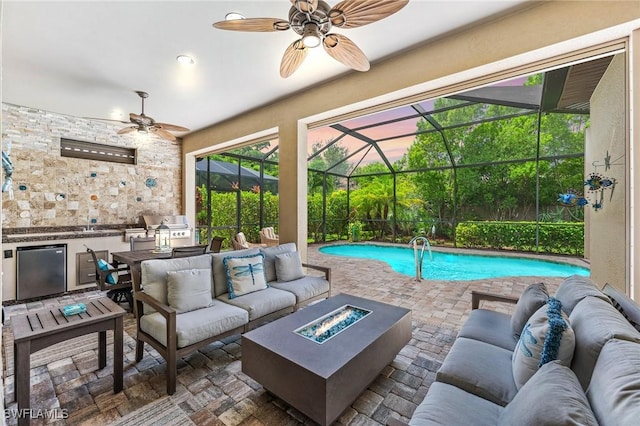 exterior space featuring glass enclosure, an outdoor living space with a fire pit, exterior kitchen, ceiling fan, and a patio area