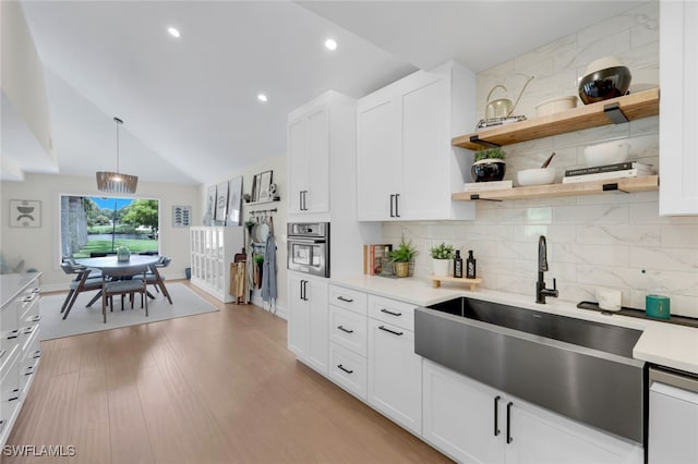 kitchen featuring white cabinetry, sink, hanging light fixtures, oven, and light wood-type flooring