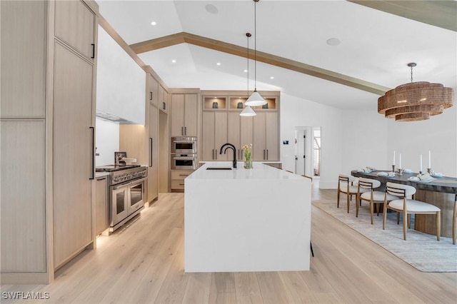 kitchen with vaulted ceiling with beams, a kitchen island with sink, a sink, light wood-style floors, and appliances with stainless steel finishes