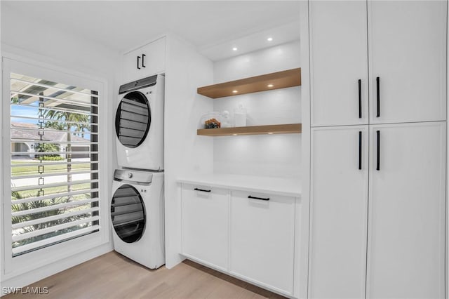 laundry area featuring cabinet space, recessed lighting, light wood finished floors, and stacked washer and clothes dryer