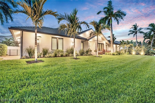 view of front of house featuring stucco siding, fence, and a yard