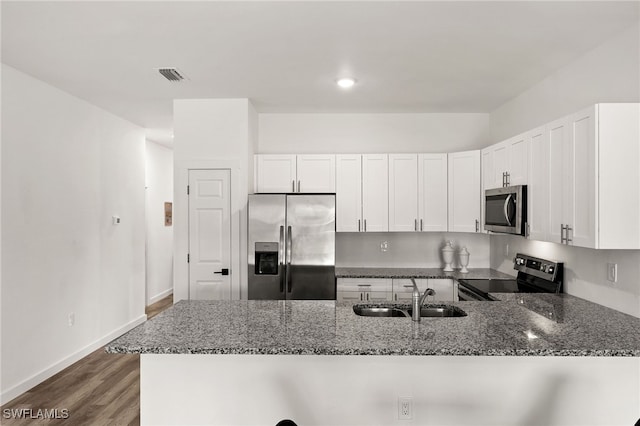 kitchen featuring appliances with stainless steel finishes, white cabinetry, sink, dark hardwood / wood-style floors, and dark stone counters