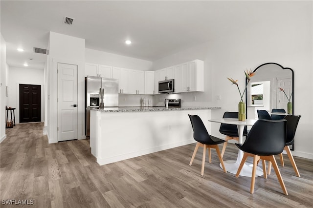 kitchen featuring appliances with stainless steel finishes, kitchen peninsula, white cabinets, and light hardwood / wood-style floors