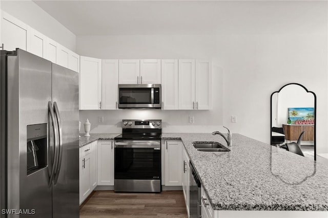 kitchen with light stone counters, kitchen peninsula, sink, dark hardwood / wood-style floors, and appliances with stainless steel finishes