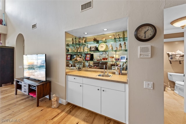 bar featuring light wood-type flooring, white cabinetry, and sink