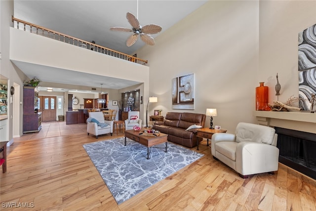 living room featuring ceiling fan, light hardwood / wood-style floors, and a towering ceiling