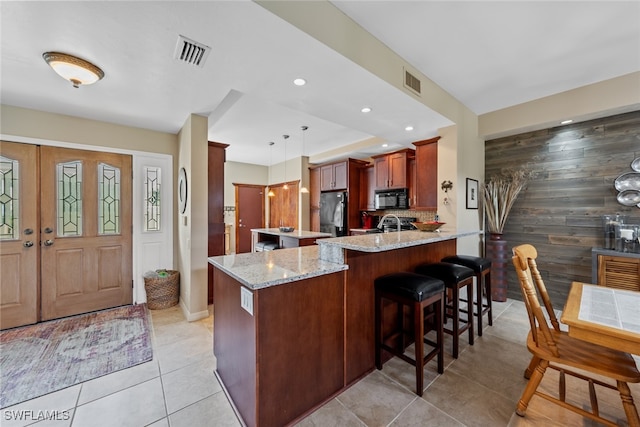 kitchen with stainless steel refrigerator, kitchen peninsula, light stone countertops, hanging light fixtures, and a breakfast bar area