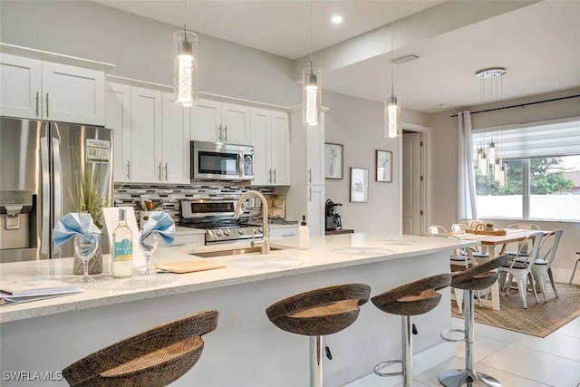 kitchen featuring white cabinetry, light stone countertops, stainless steel appliances, a kitchen bar, and decorative backsplash