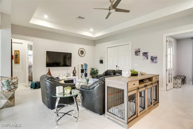 living room featuring ceiling fan, a raised ceiling, and light tile patterned floors