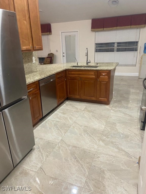 kitchen featuring tasteful backsplash, kitchen peninsula, sink, appliances with stainless steel finishes, and light stone counters