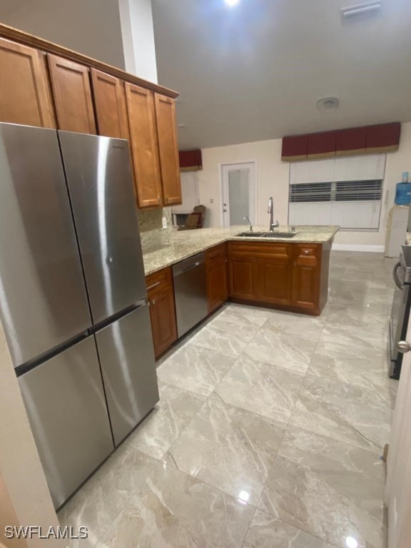 kitchen with appliances with stainless steel finishes, sink, light stone countertops, and kitchen peninsula