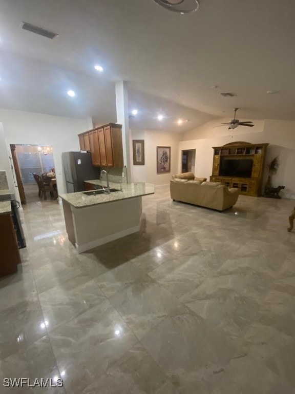 kitchen with ceiling fan, stainless steel refrigerator, vaulted ceiling, light stone counters, and sink