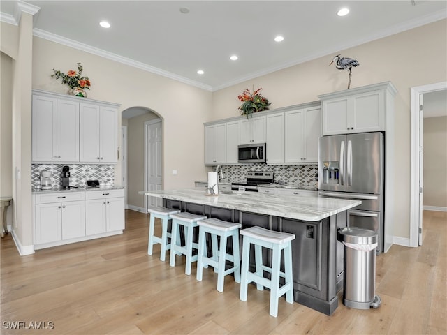 kitchen featuring light stone countertops, appliances with stainless steel finishes, a large island, white cabinets, and a breakfast bar