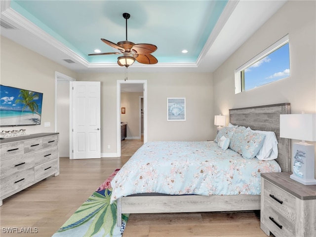 bedroom featuring crown molding, light hardwood / wood-style flooring, ceiling fan, a raised ceiling, and connected bathroom