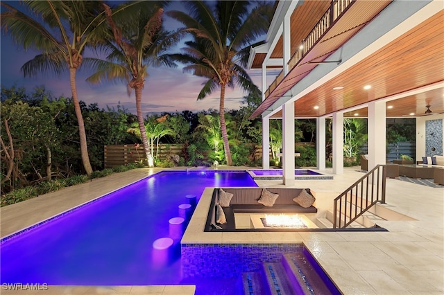 pool at dusk with a patio area, an outdoor living space, and a hot tub