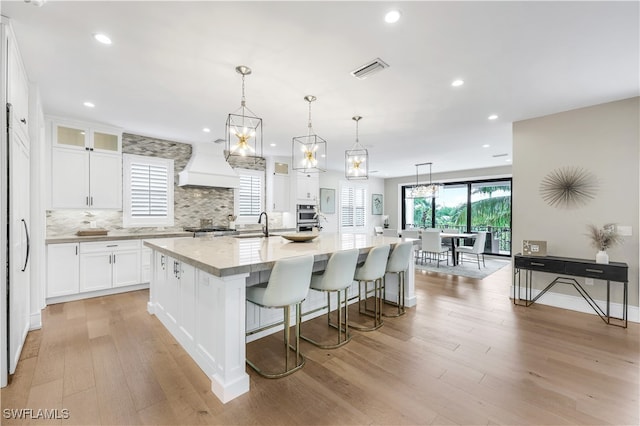 kitchen featuring custom exhaust hood, white cabinets, a spacious island, hanging light fixtures, and light hardwood / wood-style floors