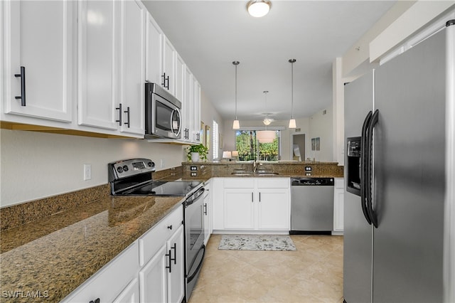 kitchen featuring kitchen peninsula, hanging light fixtures, dark stone countertops, appliances with stainless steel finishes, and white cabinetry