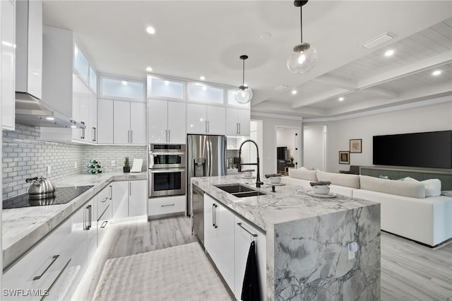 kitchen featuring sink, hanging light fixtures, wall chimney exhaust hood, an island with sink, and beam ceiling