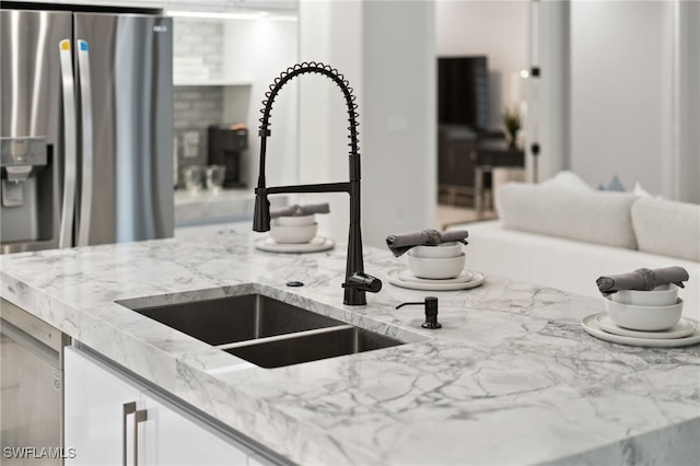 room details with stainless steel fridge with ice dispenser, light stone counters, and sink