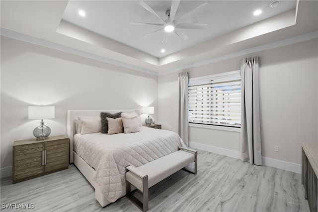 bedroom with a raised ceiling, ceiling fan, and light hardwood / wood-style flooring